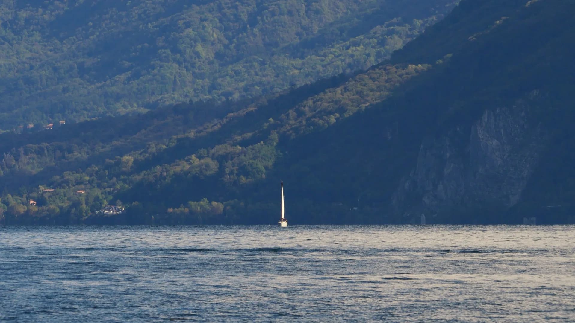 A small sailboat beneath the wooded mountains of Lago Maggiore