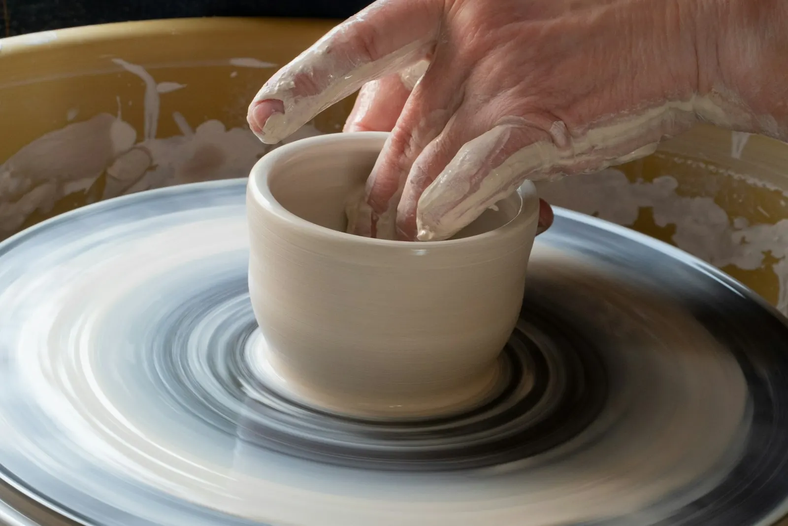 A potter's hands shaping a cup on the wheel.